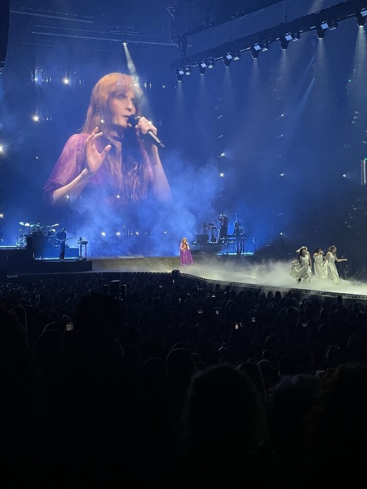 Florence Welch singing with arms outstretched at a Florence + the Machine concert